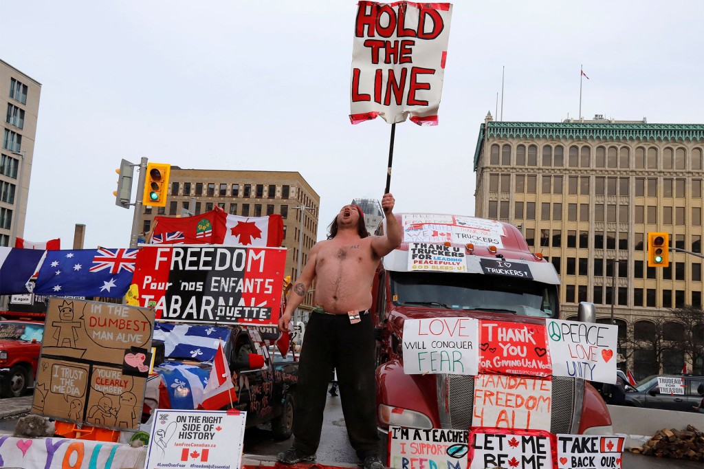 Eine Person hält ein Schild vor Lastwagen, die eine Straße in der Innenstadt blockieren, während Lastwagenfahrer und ihre Unterstützer weiterhin gegen Vorschriften für einen Impfstoff gegen das Coronavirus (COVID-19) in Ottawa, Ontario, Kanada, protestieren.