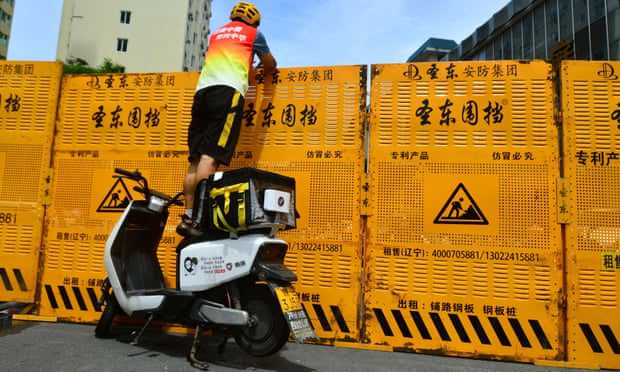 Ein Kurier, der auf einem Elektrofahrrad steht, um Waren über eine Straßensperre in Sanya, Provinz Hainan, zu liefern