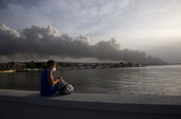Ein Anwohner sitzt auf der Malecon-Dammmauer, während Rauch vom Feuer im Hintergrund aufsteigt.