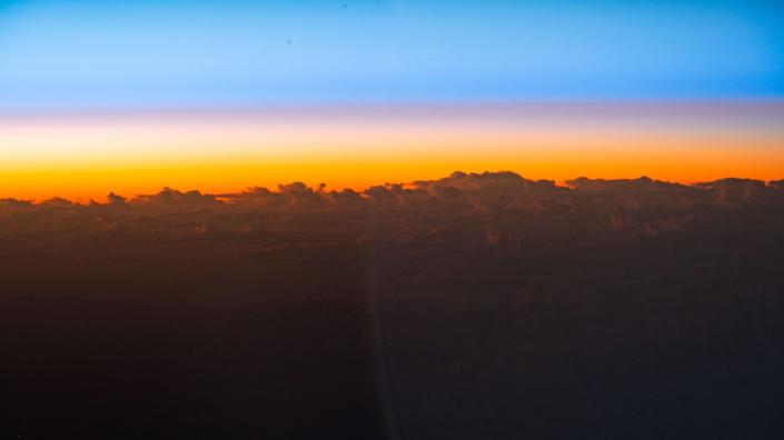 Sonnenaufgang im orangefarbenen Himmel späht über Wolkenspitzen