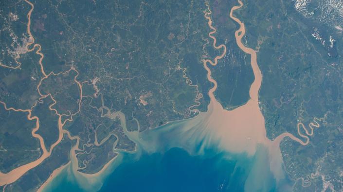 Ein Blick aus dem Weltraum, der braune Flüsse zeigt, die durch die grüne Landschaft in einen blauen Ozean fließen