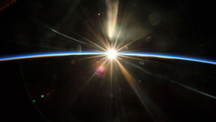 Sunrise durchdringt die Schwärze des Weltraums vor der dunklen Krümmung der Erde mit einer dünnen blauen Linie der Atmosphäre während des Tages am Horizont