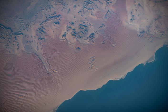 Roter Wüstensand mit fernen Bergen vor dem tiefblauen Ozean