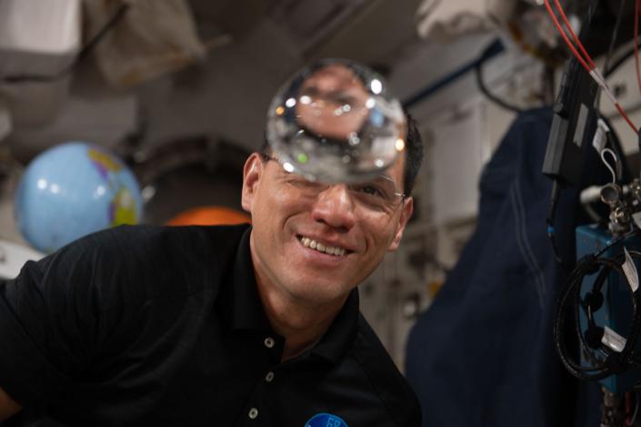 Ein Astronaut betrachtet eine schwimmende Wasserblase auf der Internationalen Raumstation
